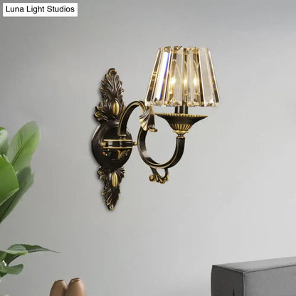 Antique brass wall light featuring a tiered crystal prism shade in a contemporary wall mounted bedroom sconce design