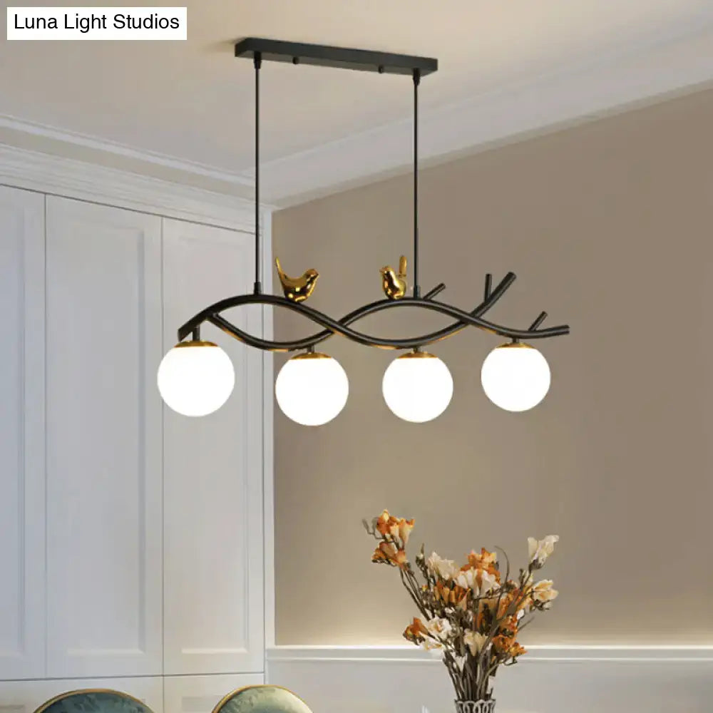 Black metal DecorBites™ linear branch dining chandelier with gold bird accents and four cream glass ball bulbs for dining room island
