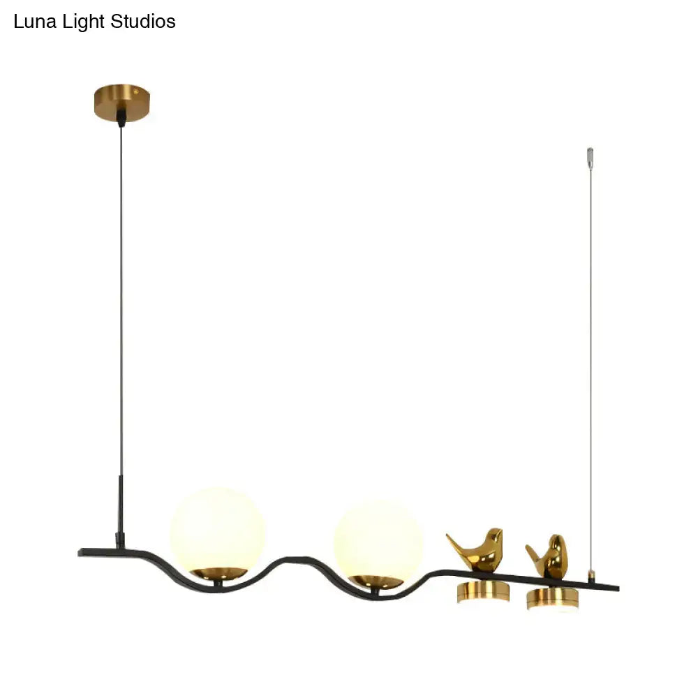 Gold-toned bird figurines adorn a black metal DecorBites linear branch dining pendant with four cream glass shades