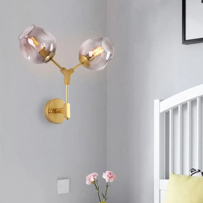 Contemporary gold-toned wall sconce with two frosted globe shades and clear glass shade for bedroom light wall use