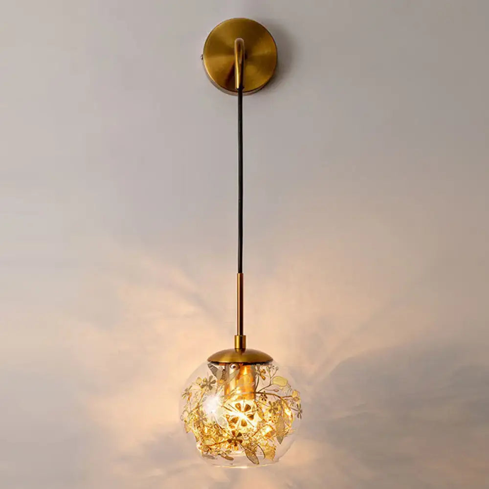 Contemporary brass clear glass wall lamp with foil flower decor and gold accents suspended by black cord for bedroom