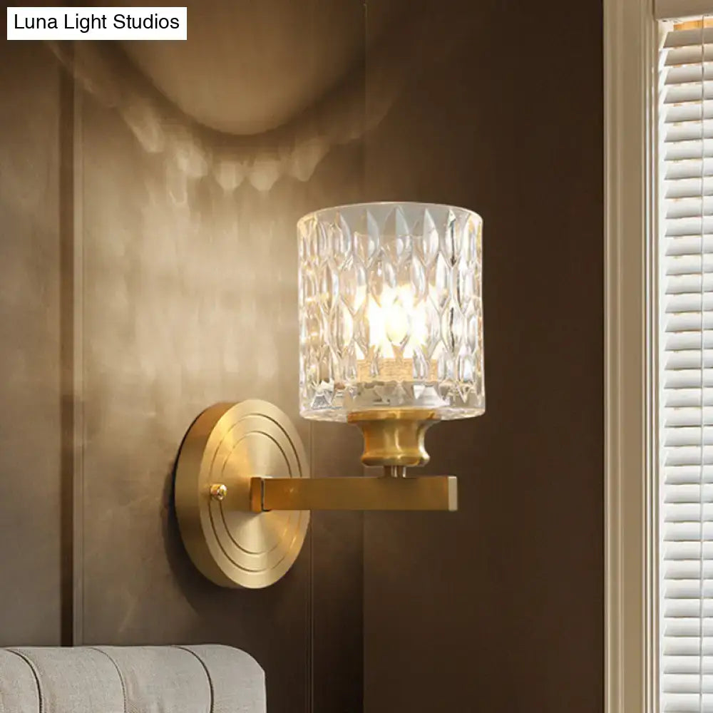 Contemporary brass cylindrical wall light with faceted clear dimpled glass shade for bedroom use