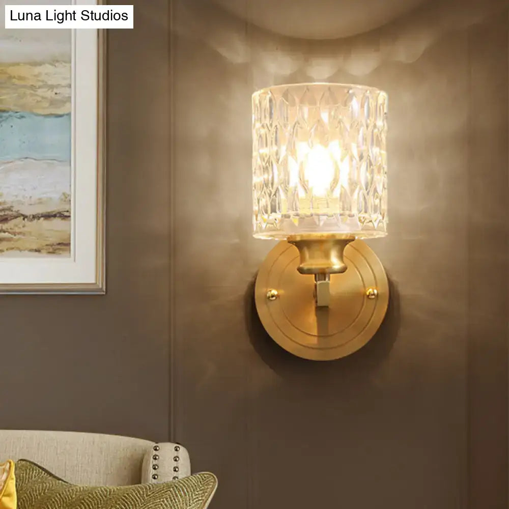 Contemporary brass cylindrical wall light with warm-toned brass finish and clear dimpled faceted glass shade for bedroom