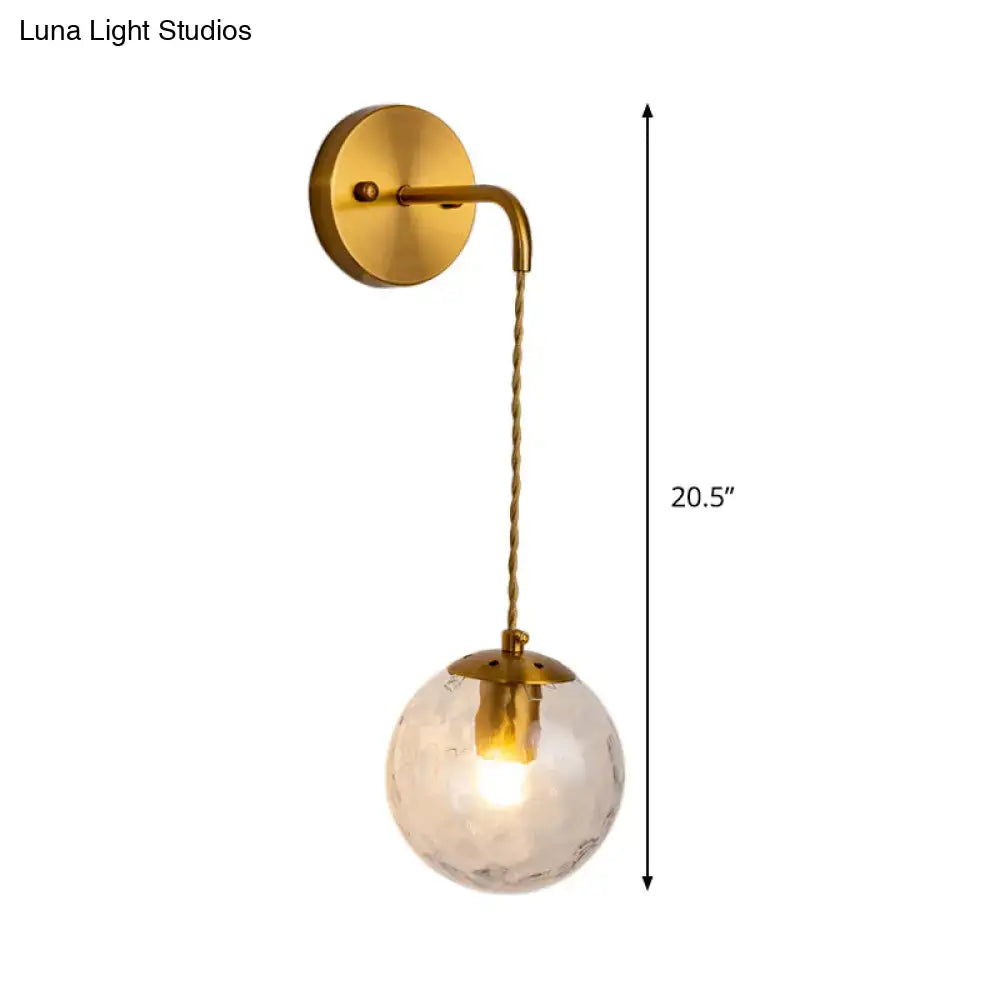 Contemporary brass wall lamp featuring a dimpled glass globe hanging from a twisted cord light fixture