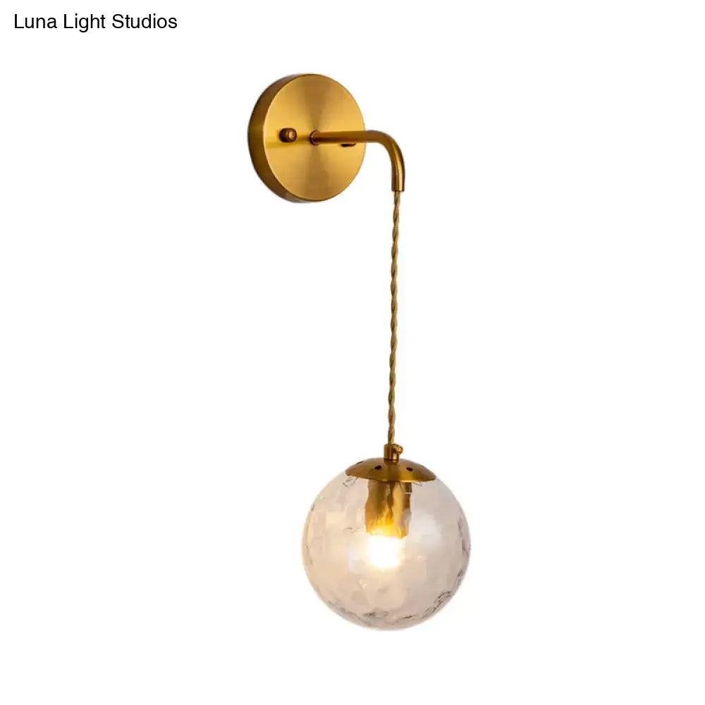 Contemporary brass wall lamp featuring a dimpled clear glass globe fixture type hanging from a twisted cord