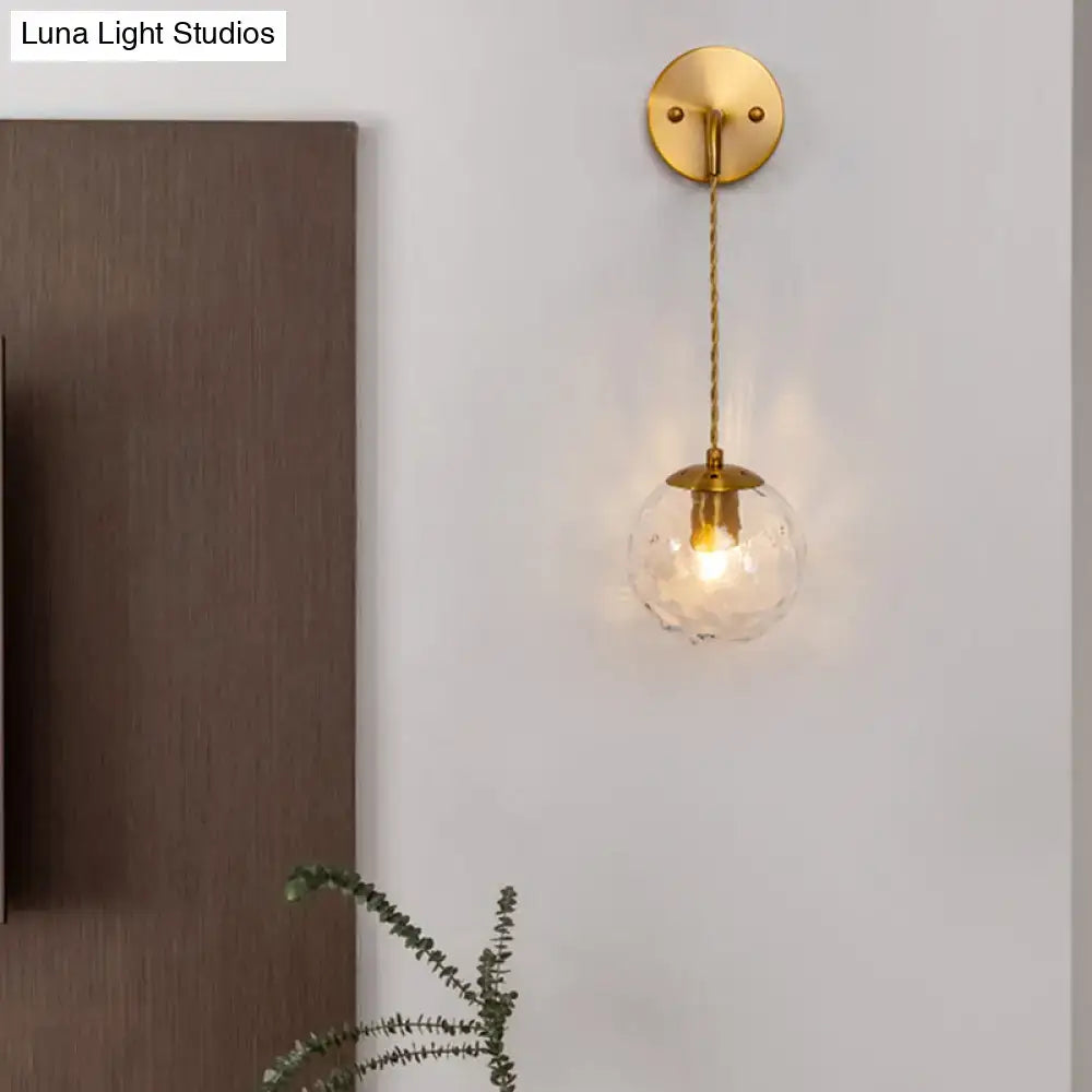 Contemporary gold-toned brass wall lamp featuring a dimpled glass globe and braided cord bedroom sconce fixture type