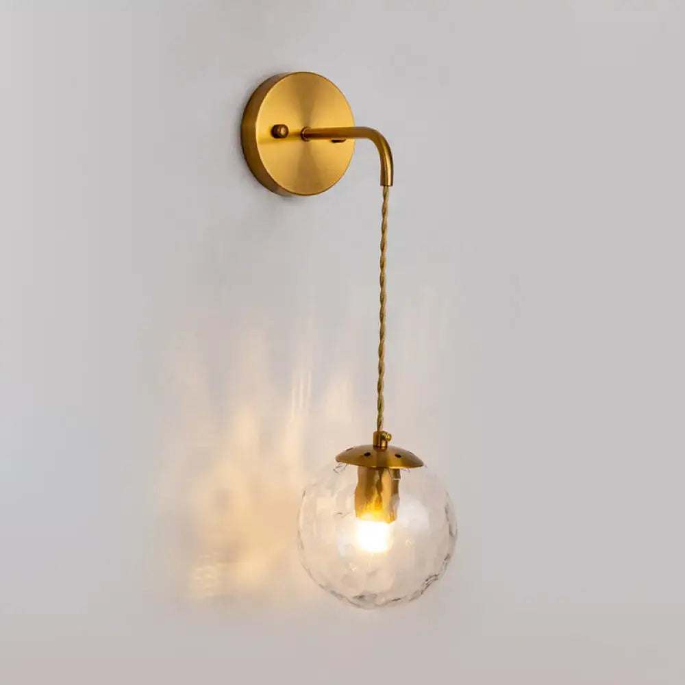 A warm-toned contemporary brass wall lamp with a dimpled glass globe and twisted cord fixture type for bedroom use