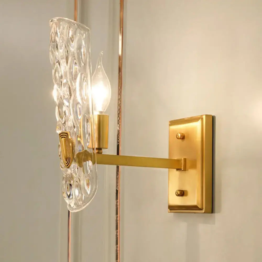 Contemporary brass wall sconce with clear water glass shade featuring textured bubble pattern for bedroom bedside light