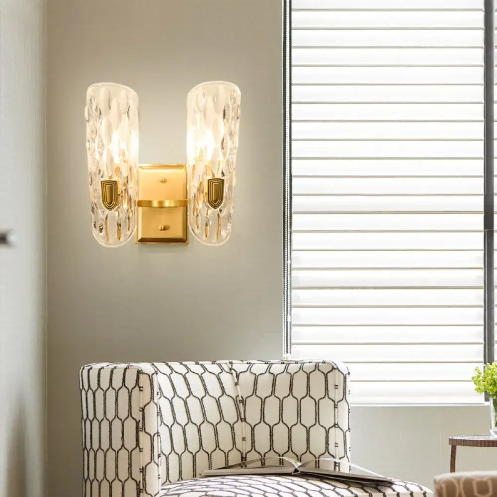 Contemporary brass wall sconce with gold-toned finish and clear water glass textured translucent shades for bedroom