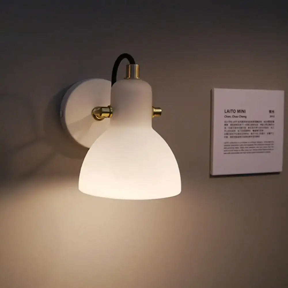 Contemporary wall lamp with white glass domed shade, brass accents, black cord, and adjustable arm for bedroom use