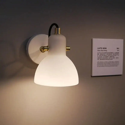 Contemporary wall lamp with white glass domed shade, brass accents, black cord, and adjustable arm for bedroom use