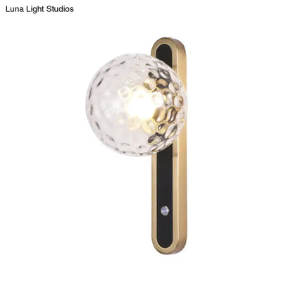 A contemporary clear glass wall lamp with textured globe and gold metal bracket showcasing fixture width