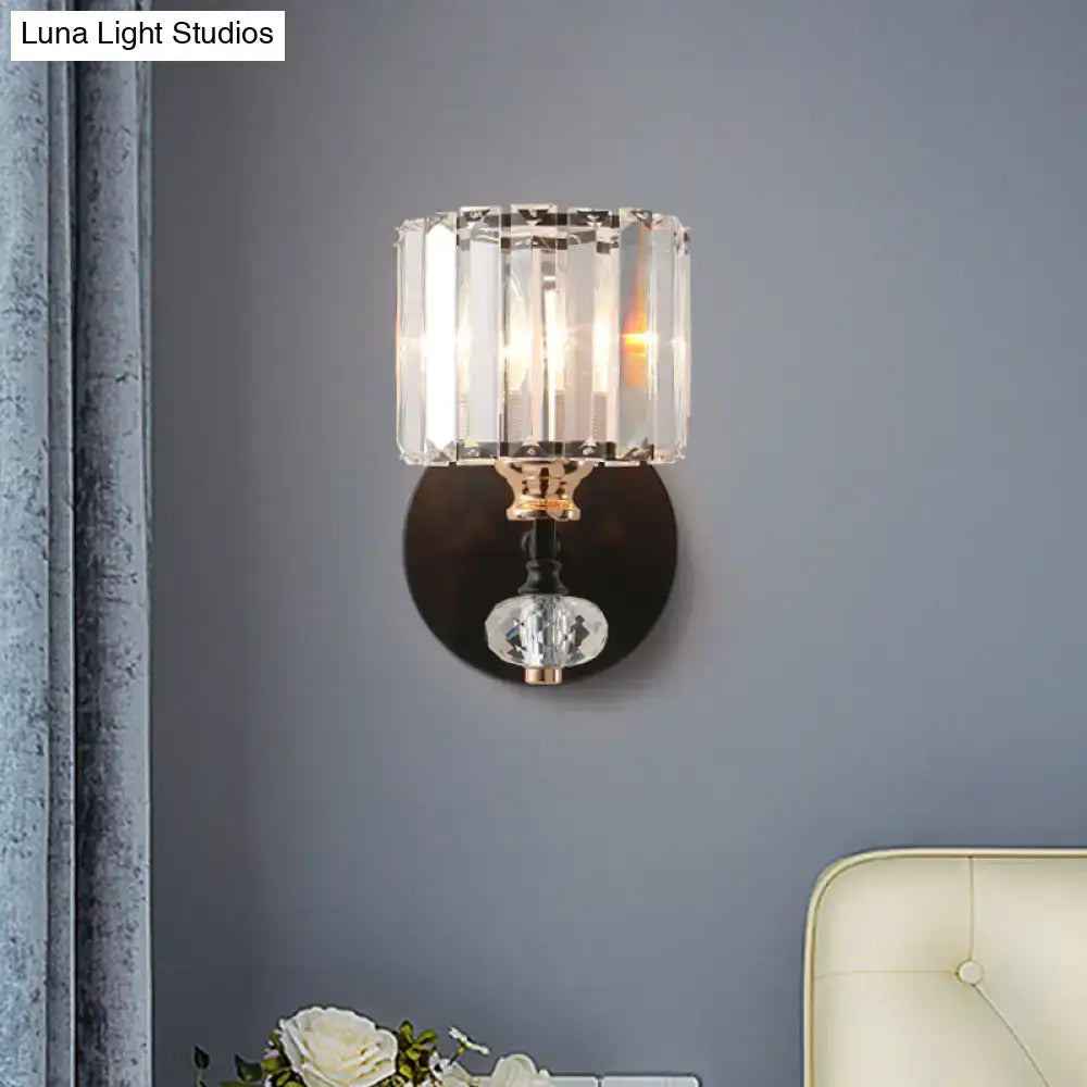 Contemporary clear ribbed glass drum sconce light with faceted cylindrical shade and polished brass base mounted on black metal