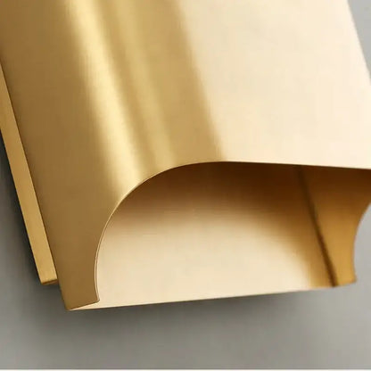 A sleek curved gold contemporary copper brass wall sconce with a smooth reflective surface for living room decorbites