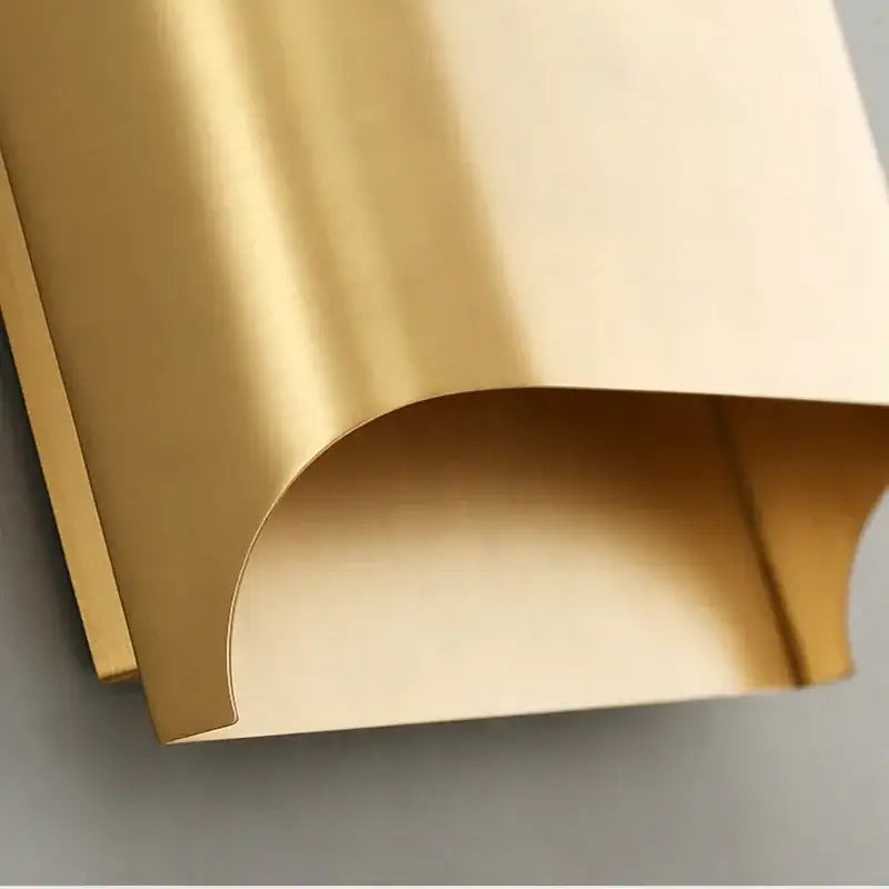 A sleek curved gold contemporary copper brass wall sconce with a smooth reflective surface for living room decorbites