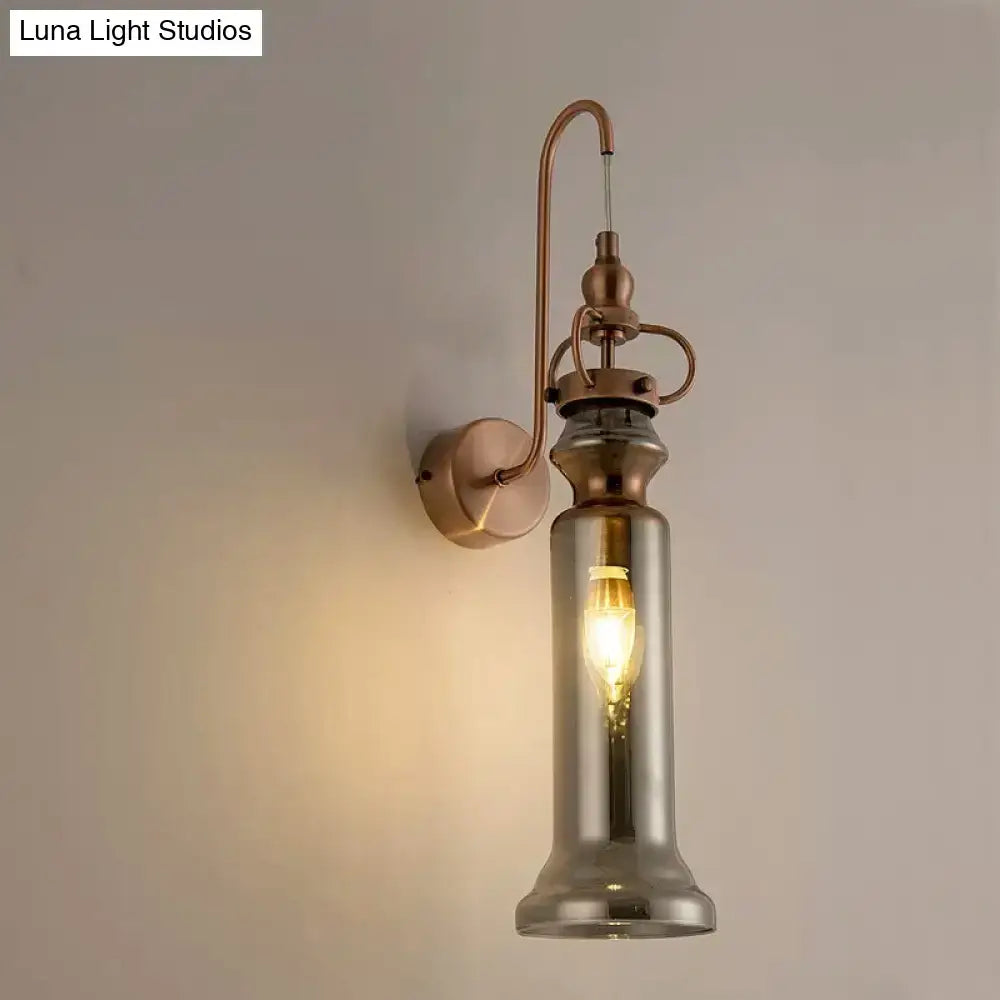Contemporary copper wall sconce with antique brass finish and tall smoked gray amber glass cylinder shade housing filament bulb