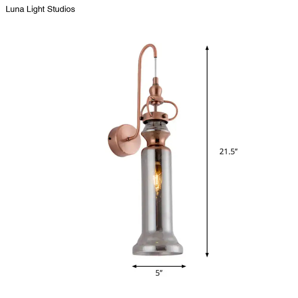 Contemporary copper wall sconce with tall cylindrical smoke gray amber glass shade and exposed filament bulb for bedroom lighting