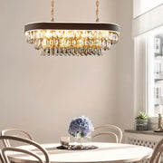 A contemporary crystal block oval island lamp light fixture with dark metal frame and gold-toned crystal droplets