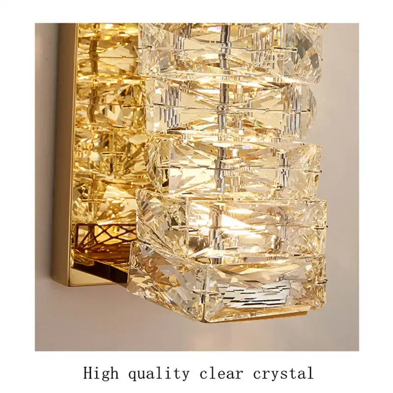 A contemporary crystal wall sconce with stacked clear crystal segments and a gold frame for bedroom decorbites lighting