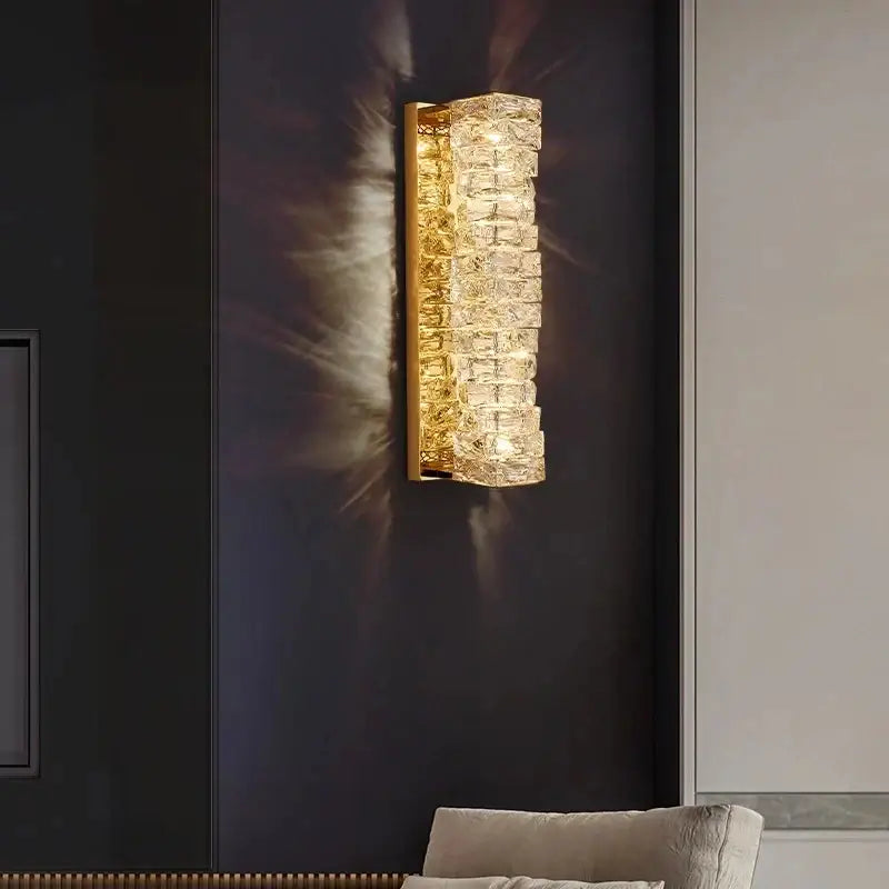 Gold-toned decorbites contemporary crystal wall sconce with stacked faceted crystals emitting warm bedroom light