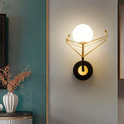 Contemporary gold-toned geometric wall sconce with cream glass orb and black base for bedroom light fixture