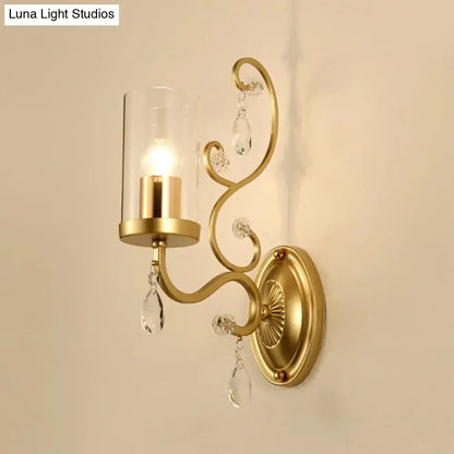 Contemporary gold wall light with clear glass cylindrical shade and crystal teardrop accents for bedroom use