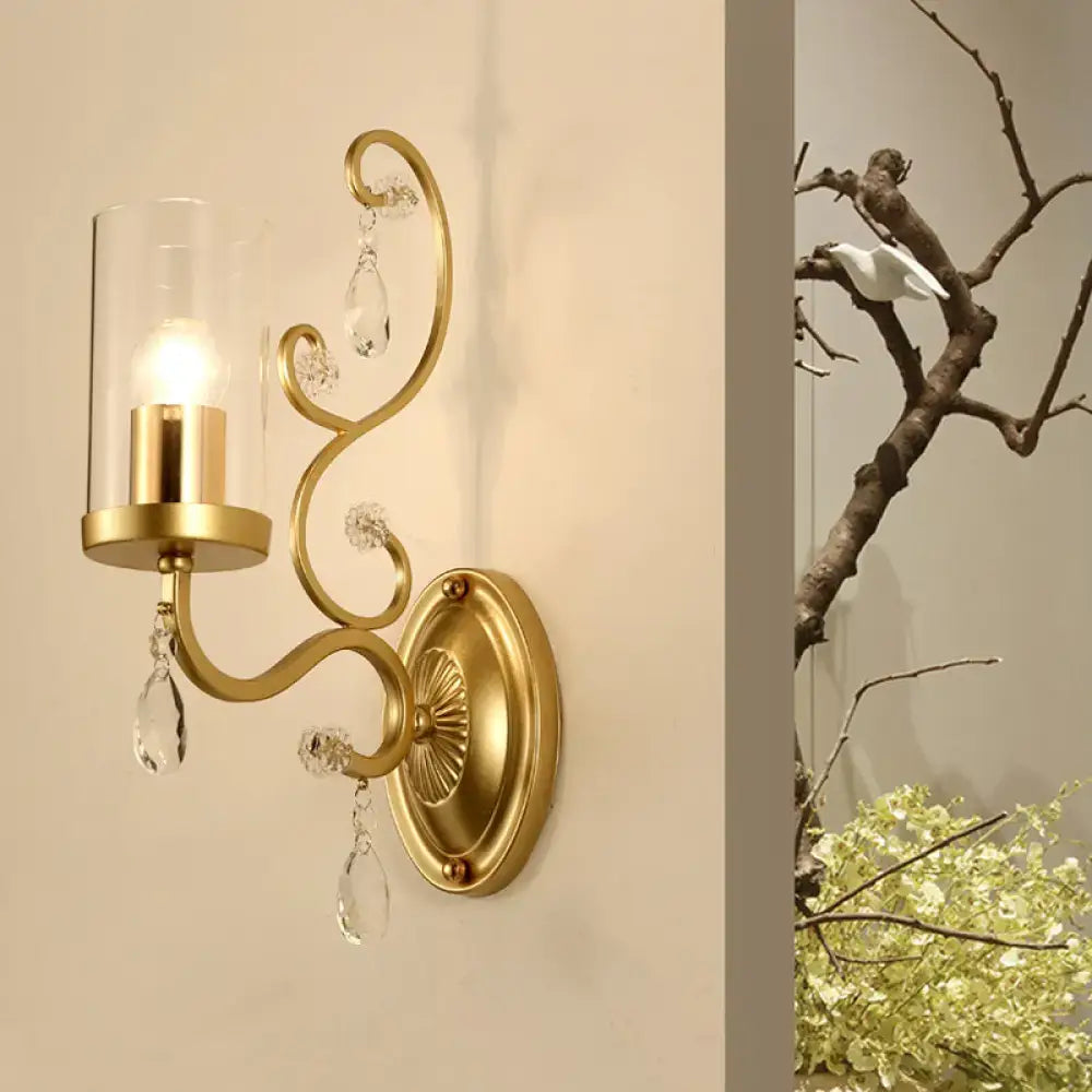 Contemporary gold wall light with clear glass cylinder, elegant curved arms, and crystal teardrop pendants for bedroom use