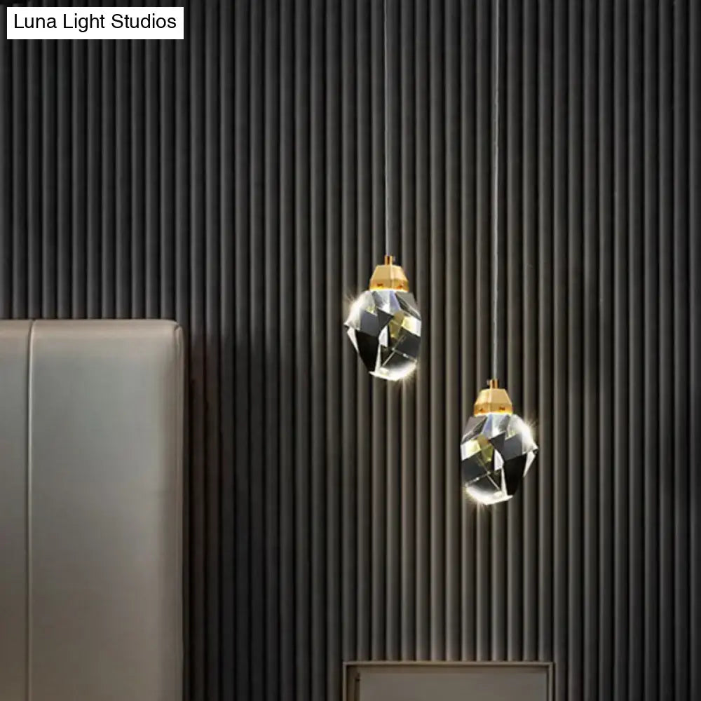 Two elegant DecorBites™ crystal stone-shape pendant light fixtures with gold tops hang against a dark ribbed wall