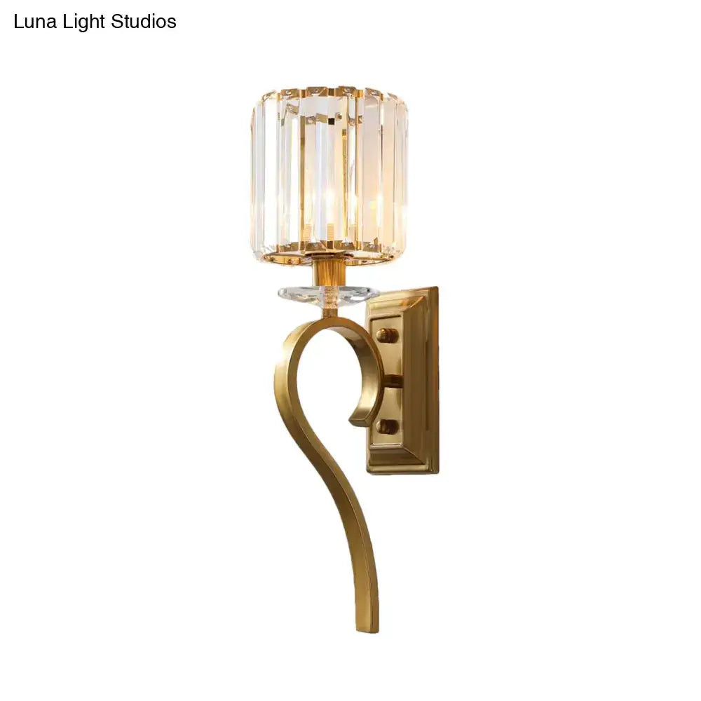 Contemporary gold cylinder wall light with a faceted crystal shade and curved metal arm for bedroom use