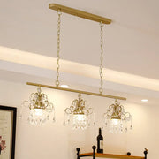 Gold-toned decorbites contemporary island chandelier with three crystal pendant lights and ornate scroll frame design