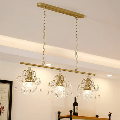 Gold-toned decorbites contemporary island chandelier with three crystal pendant lights and ornate scroll frame design
