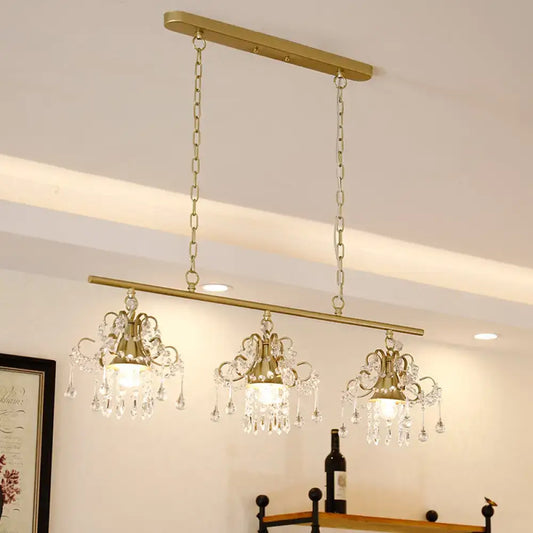 Gold-toned decorbites contemporary island chandelier with three crystal pendant lights and ornate scroll frame design