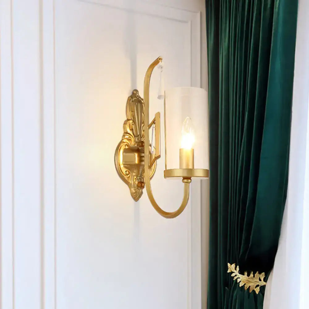 Contemporary gold wall light bedroom sconce with a gold-toned ornate design and clear glass shade with exposed bulb