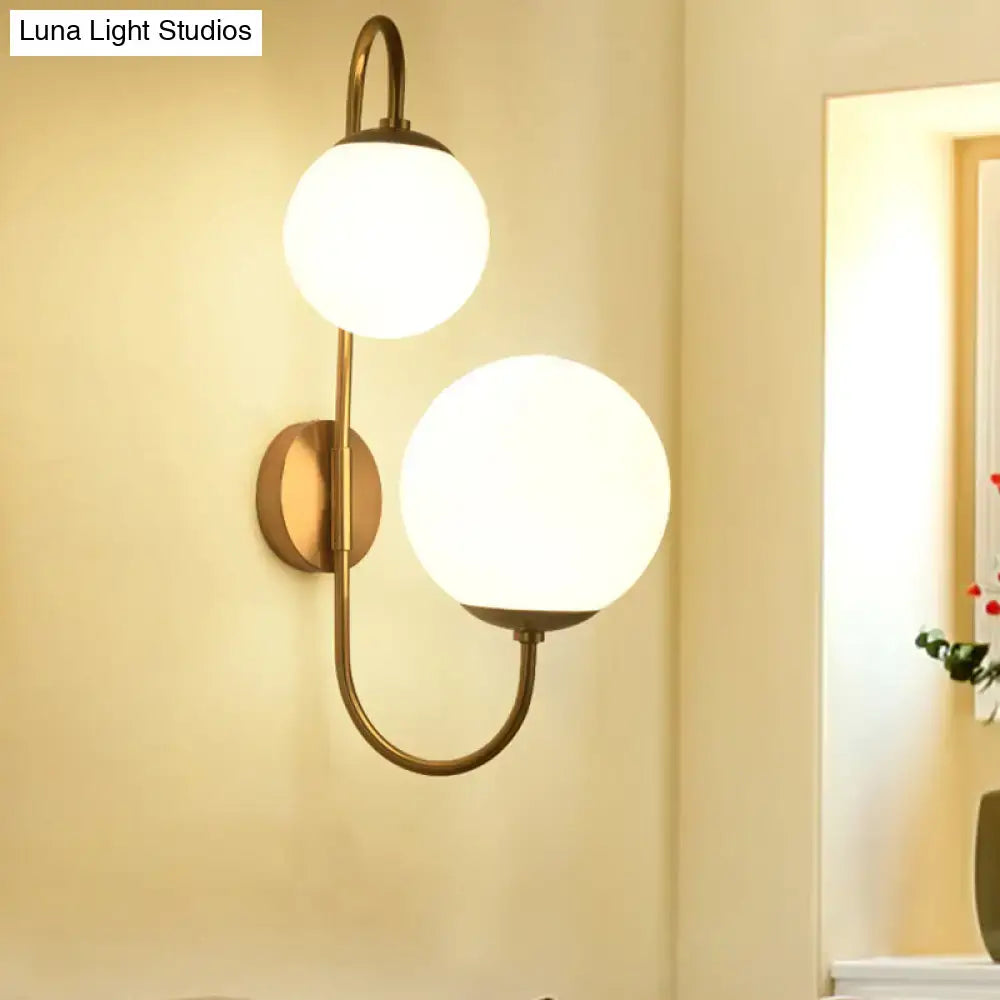 Contemporary gold wall sconce with brass finish and two spherical opal glass shade globes for bedroom lighting