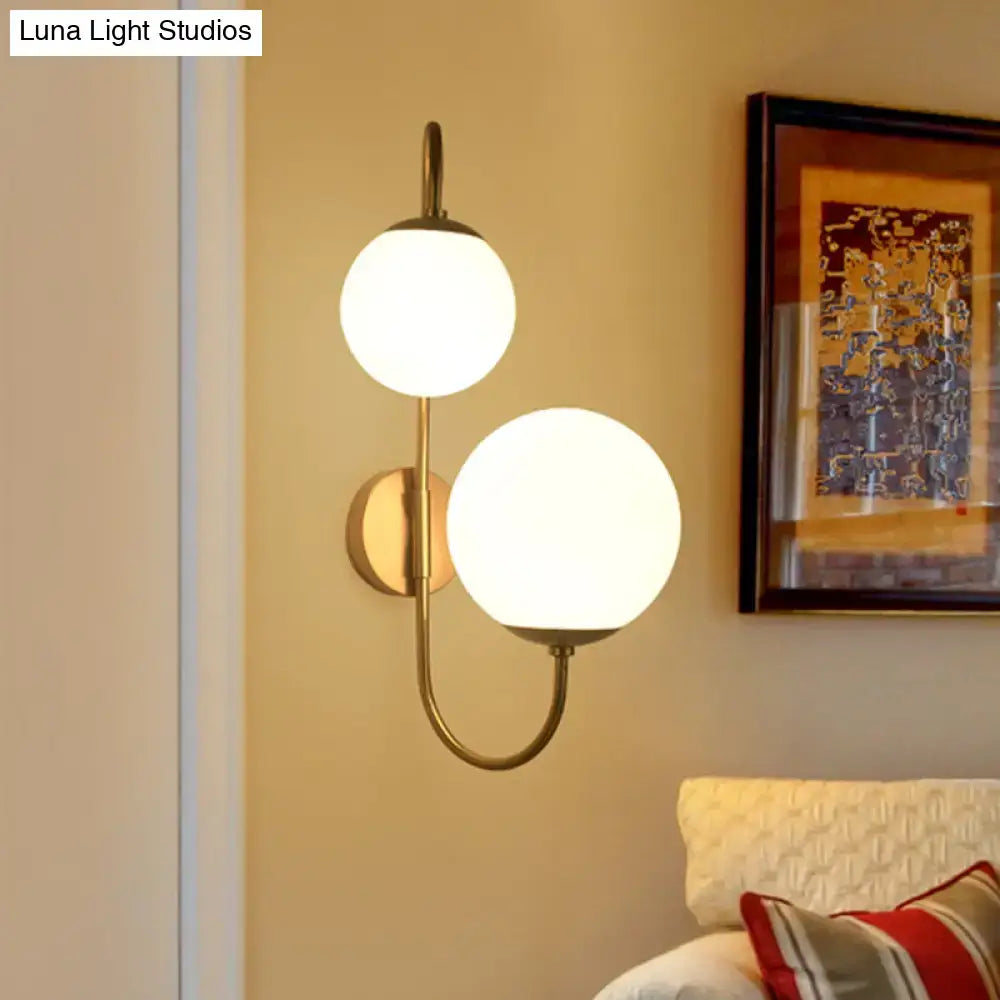 Contemporary gold wall sconce with brass finish and two spherical opal glass shades for bedroom lighting