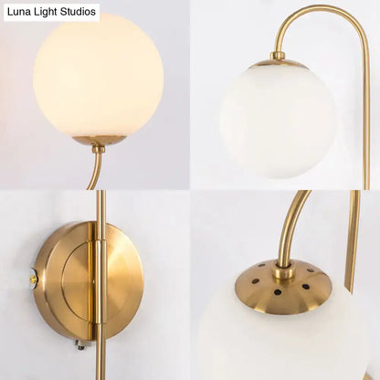 Contemporary gold wall sconce light with frosted opal glass globe and curved brass arm for bedroom lighting