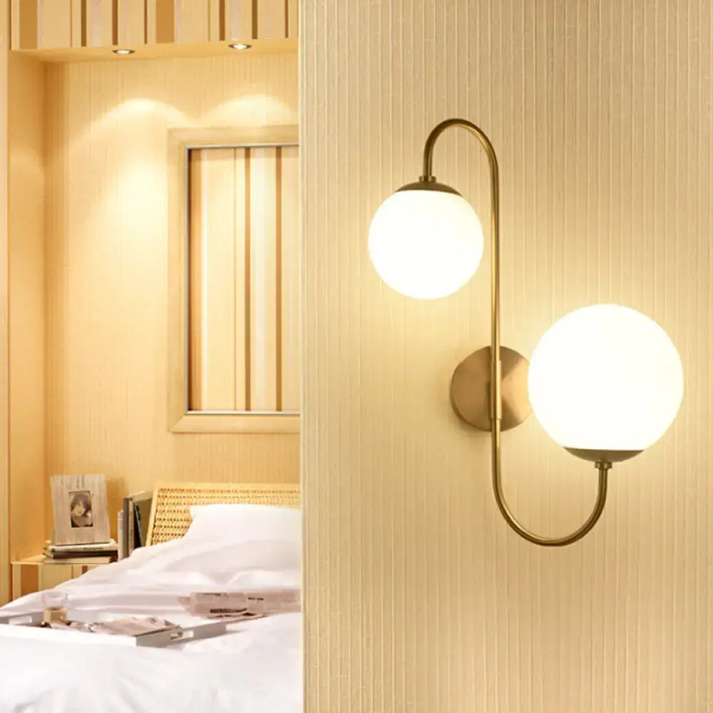 Contemporary gold wall sconce light with brass finish and two spherical frosted opal glass globes for bedroom use