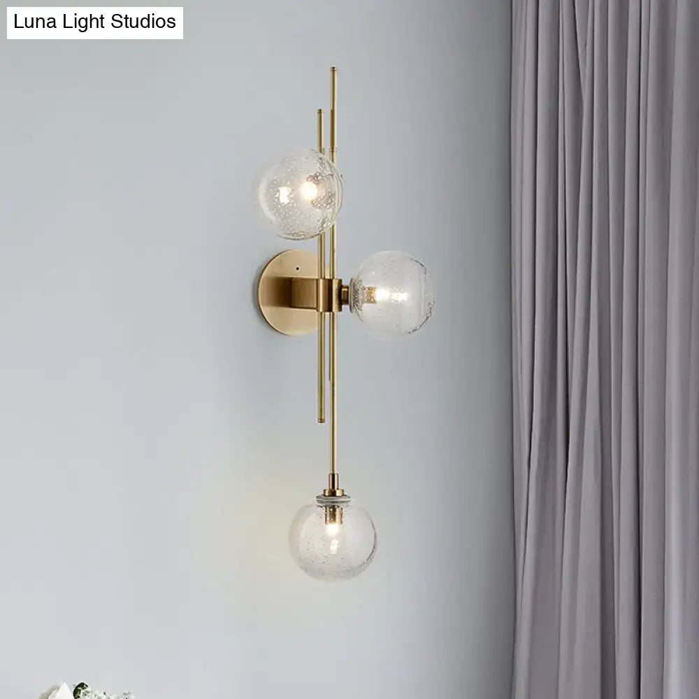 Contemporary brass-finished wall sconce with three clear glass globe shades arranged vertically for direct wired electric use