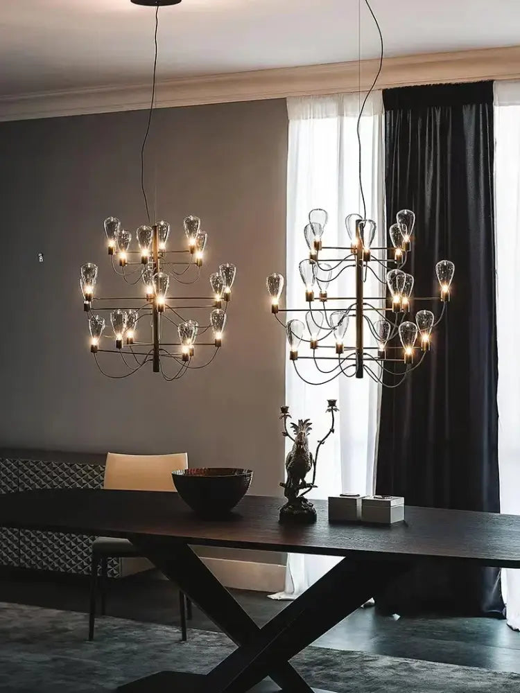 Two elegant contemporary iron glass chandeliers with exposed filament bulbs and black metal frames hang above a dining table