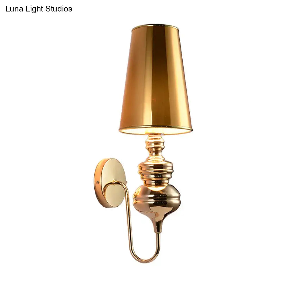 Gold-finished brass wall mount light with tapered reflective lampshade and ornate curved arm for bedroom use