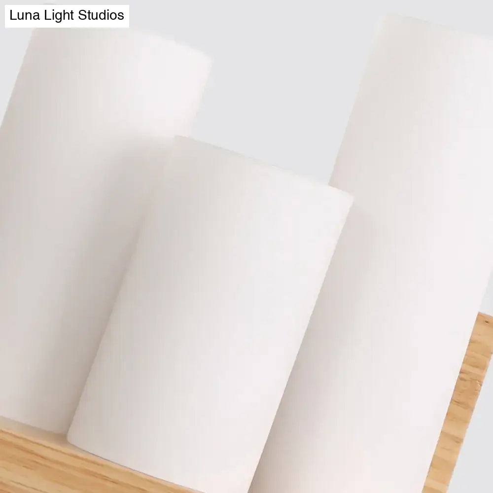 Contemporary tube shade wall lamp with wooden shelf featuring three white cylindrical matte candles on wooden surface