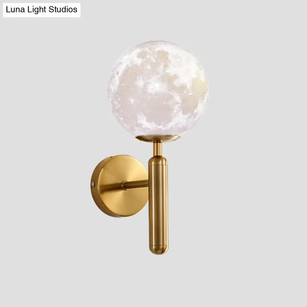 A sleek gold-toned contemporary white glass wall sconce with a textured moon-like globe for bedroom lighting