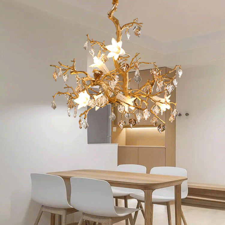 Golden tree branch chandelier with white flowers and clear crystal pendants.