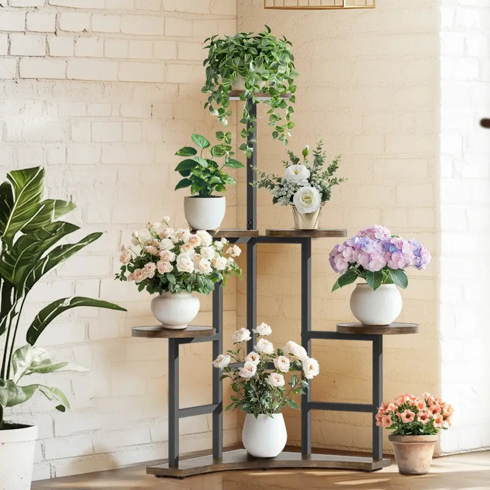 Black metal corner plant stand with wooden shelves holding white ceramic pots and floral arrangements by DecorBites™