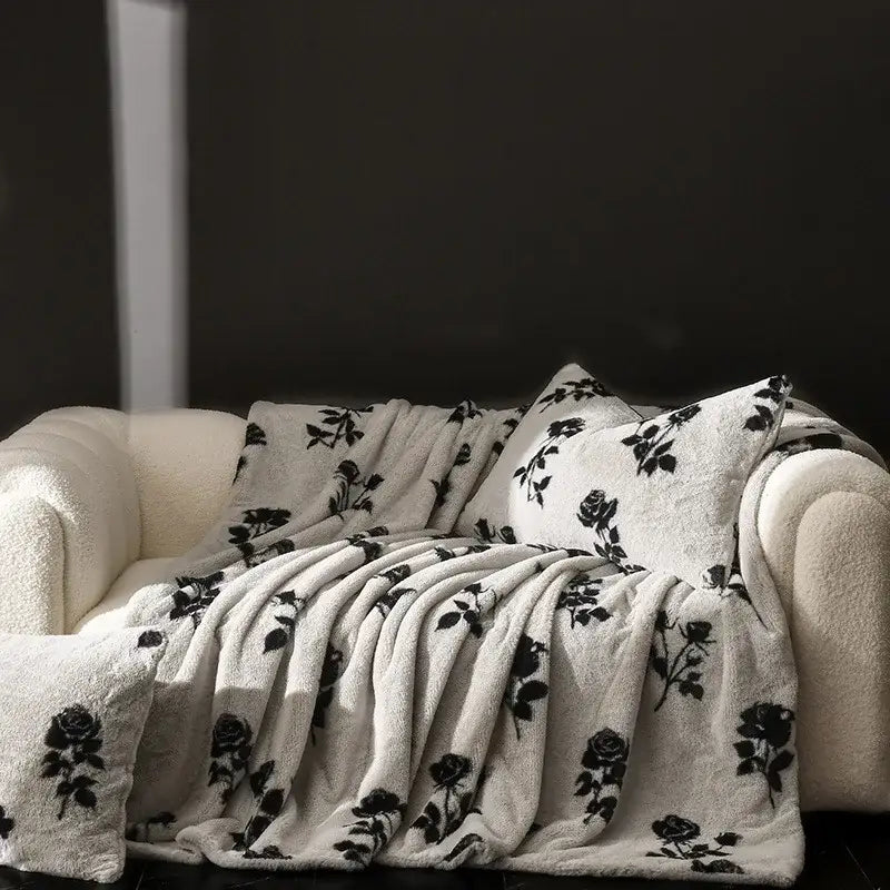 Cream-colored decorbites cosy faux rabbit plush throw blanket with black rose vine pattern draped over matching sofa