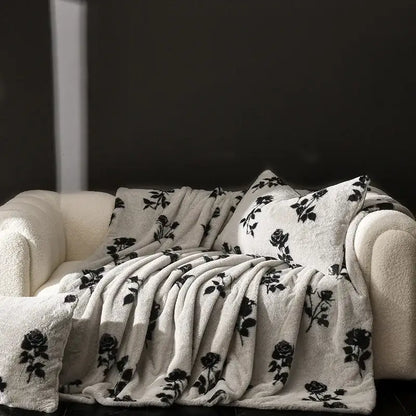 Cream-colored decorbites cosy faux rabbit plush throw blanket with black rose vine pattern draped over matching sofa