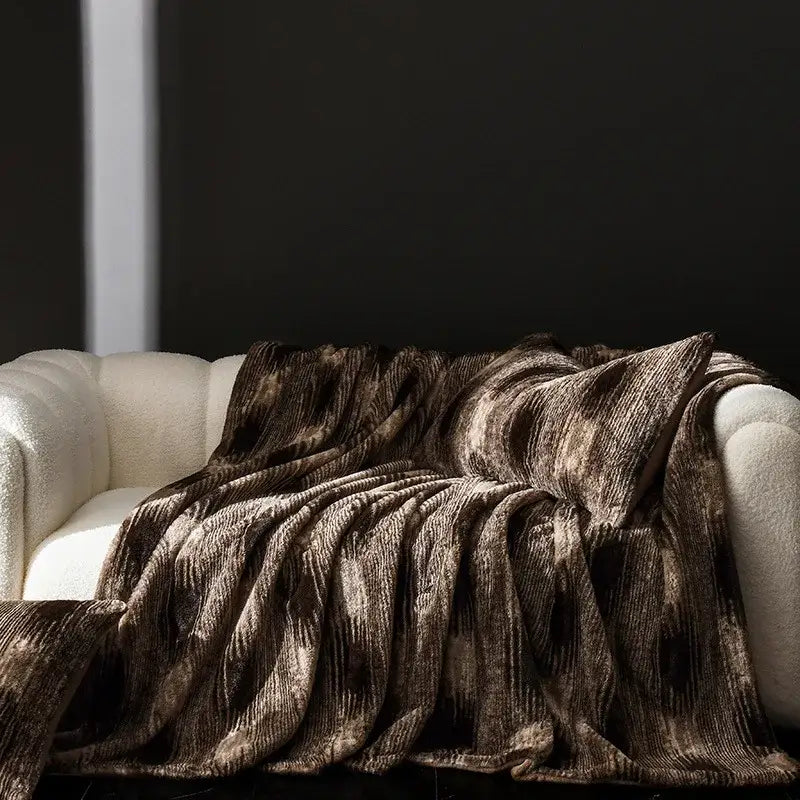 A cosy faux rabbit plush throw blanket with textured brown and black mottled pattern draped on cream sofa decorbites cosy faux