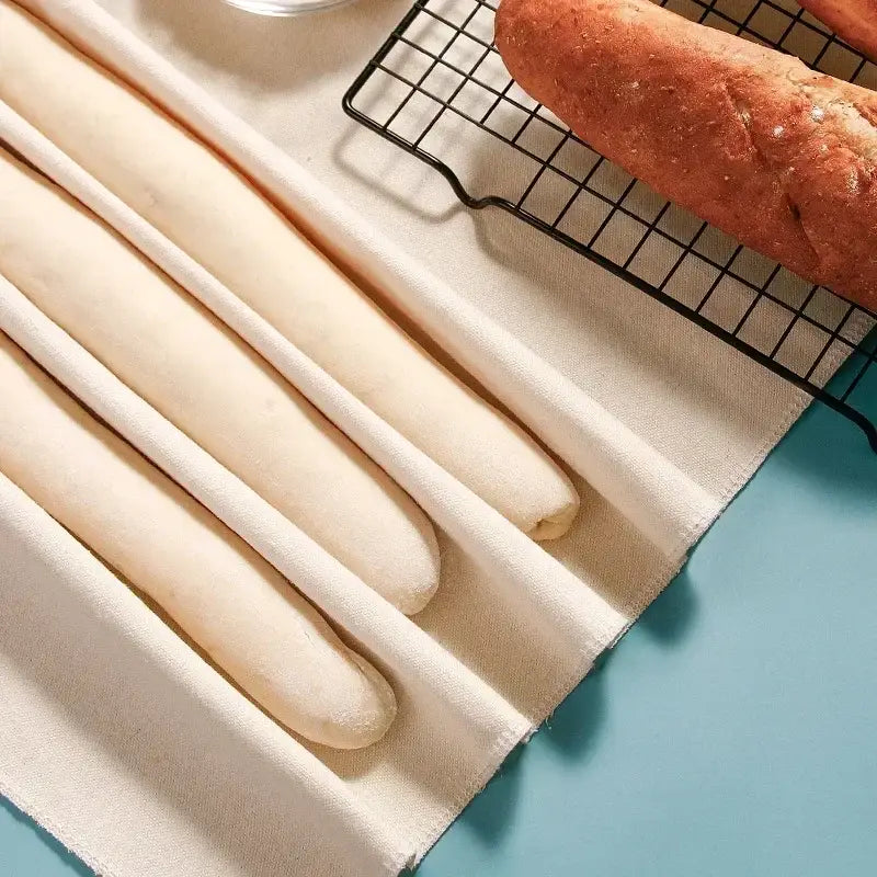 Cream-colored soft bread rolls resting in a fabric-lined baking tray using a cotton baguette proofing cloth