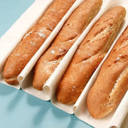 Four golden-brown baguettes in individual white cotton sleeves using a cotton baguette proofing cloth for baking
