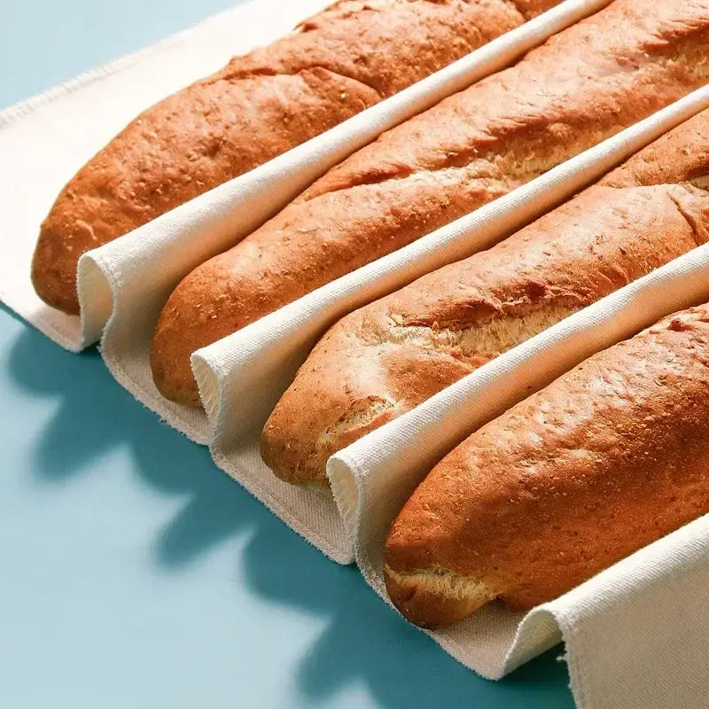 Four golden-brown crusty baguettes nestled in white cotton baguette proofing cloth baking sleeves for proofing bread